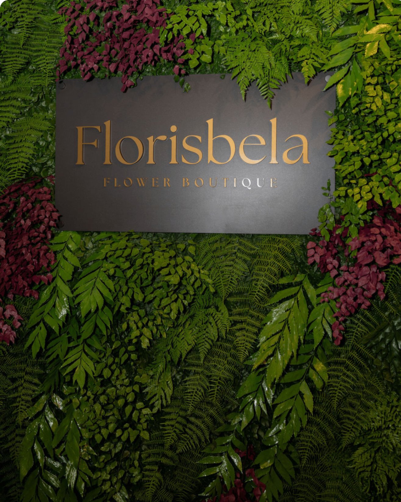 Placa do atelier Florisbela Flower Boutique em um jardim vertical exuberante.