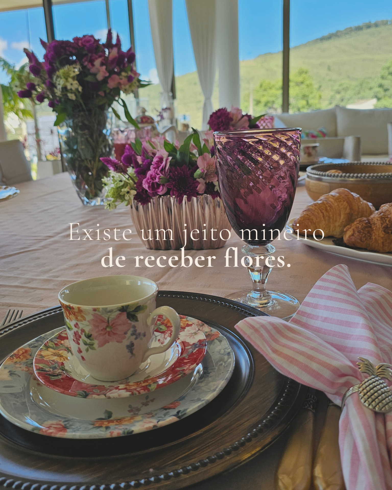 Mesa posta com louça floral, taça roxa e arranjos Florisbela.