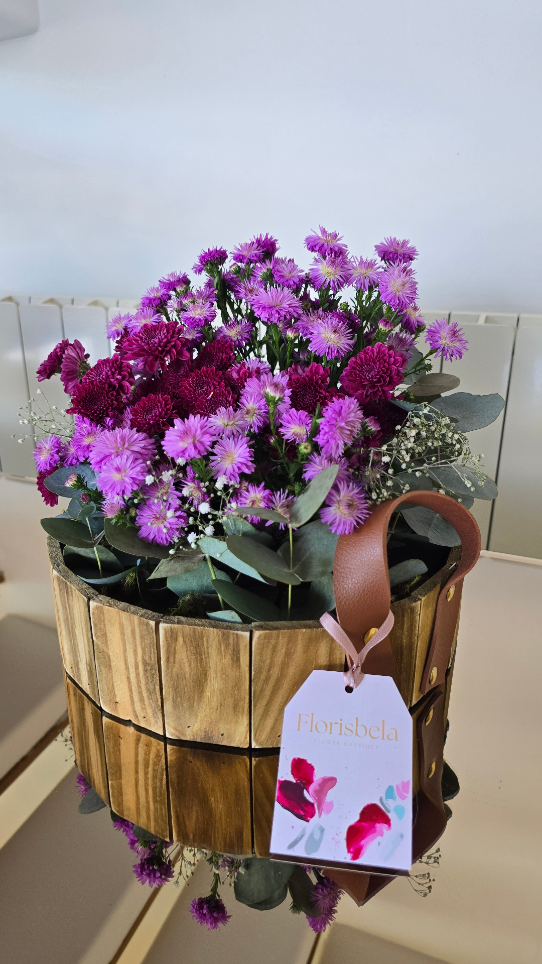 Arranjo de mesa em balde de madeira com áster lilás, crisântemos magenta e eucalipto.