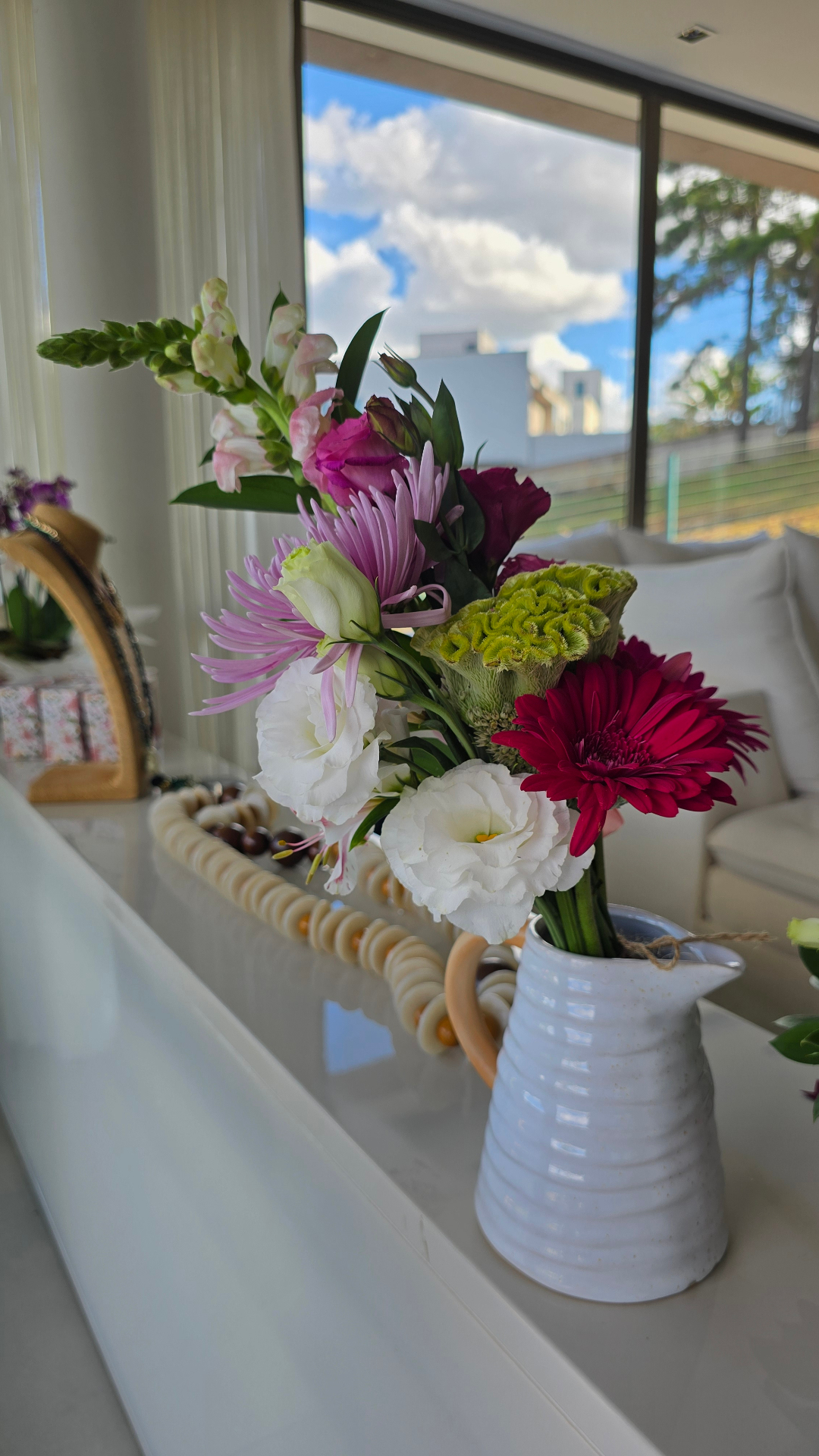 Arranjo em jarra branca de cerâmica com gérbera magenta, lisianthus brancos, celosia verde e snapdragons.