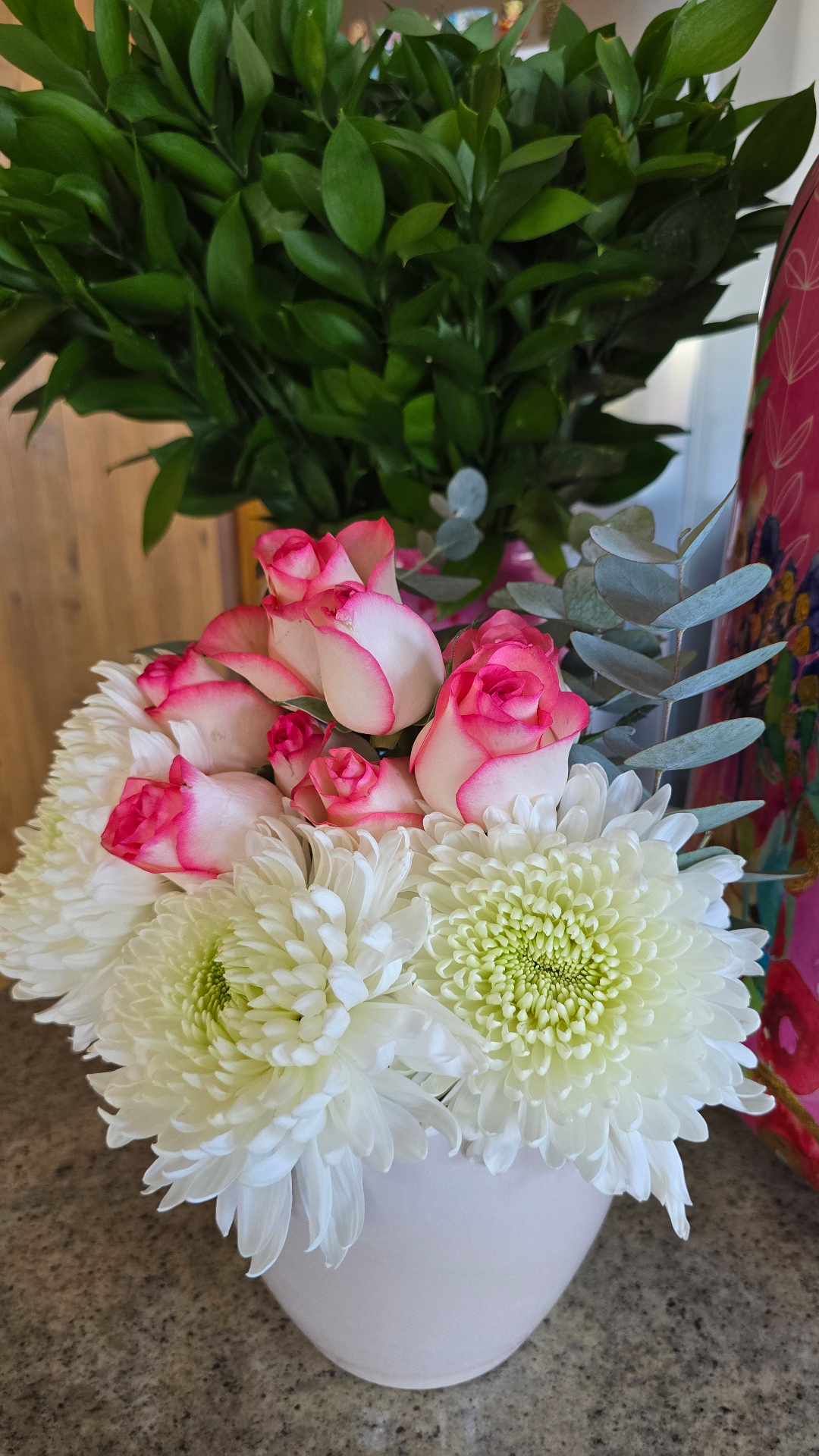 Arranjo de mesa com crisântemos brancos e rosas bicolor em vaso branco.